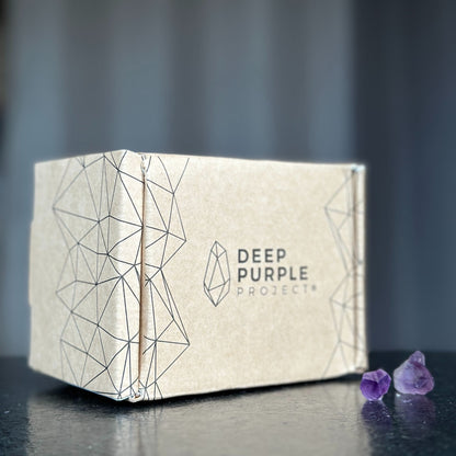 Beige box with geometric design and 'Deep Purple Project' branding on a dark surface with purple crystals.