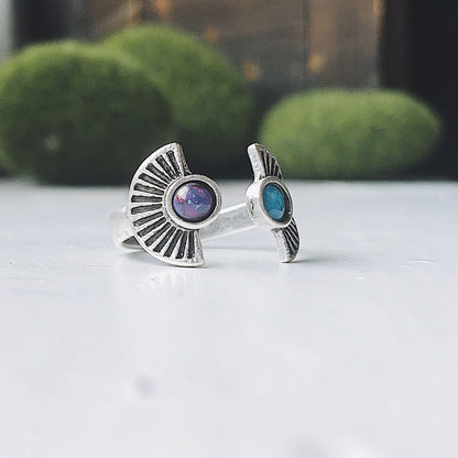 Silver rings with embedded stones on a white surface with greenery in the background