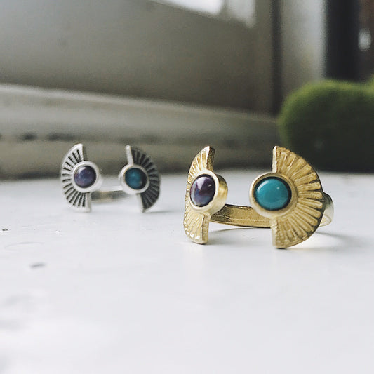 Two rings, one gold and one silver, with gemstones on a white surface.