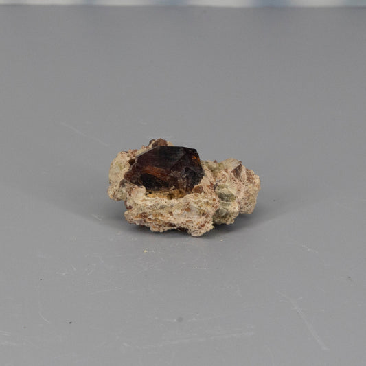 Mineral sample with a garnet crystal on a gray background