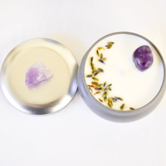 Round container candle with a purple crystal and dried herbs on a white background
