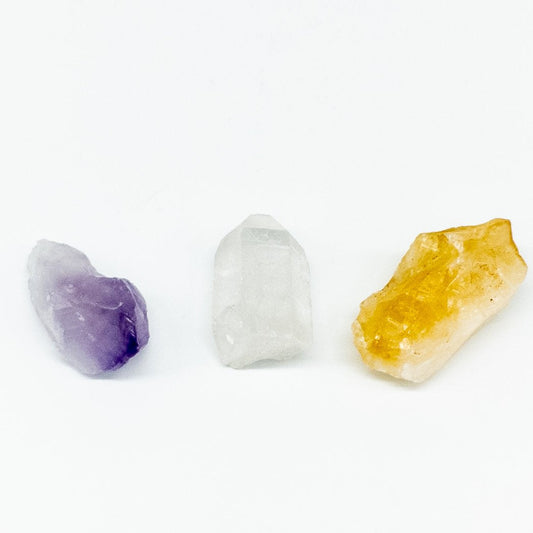 Three crystals, one purple, one white, and one yellow, on a white background