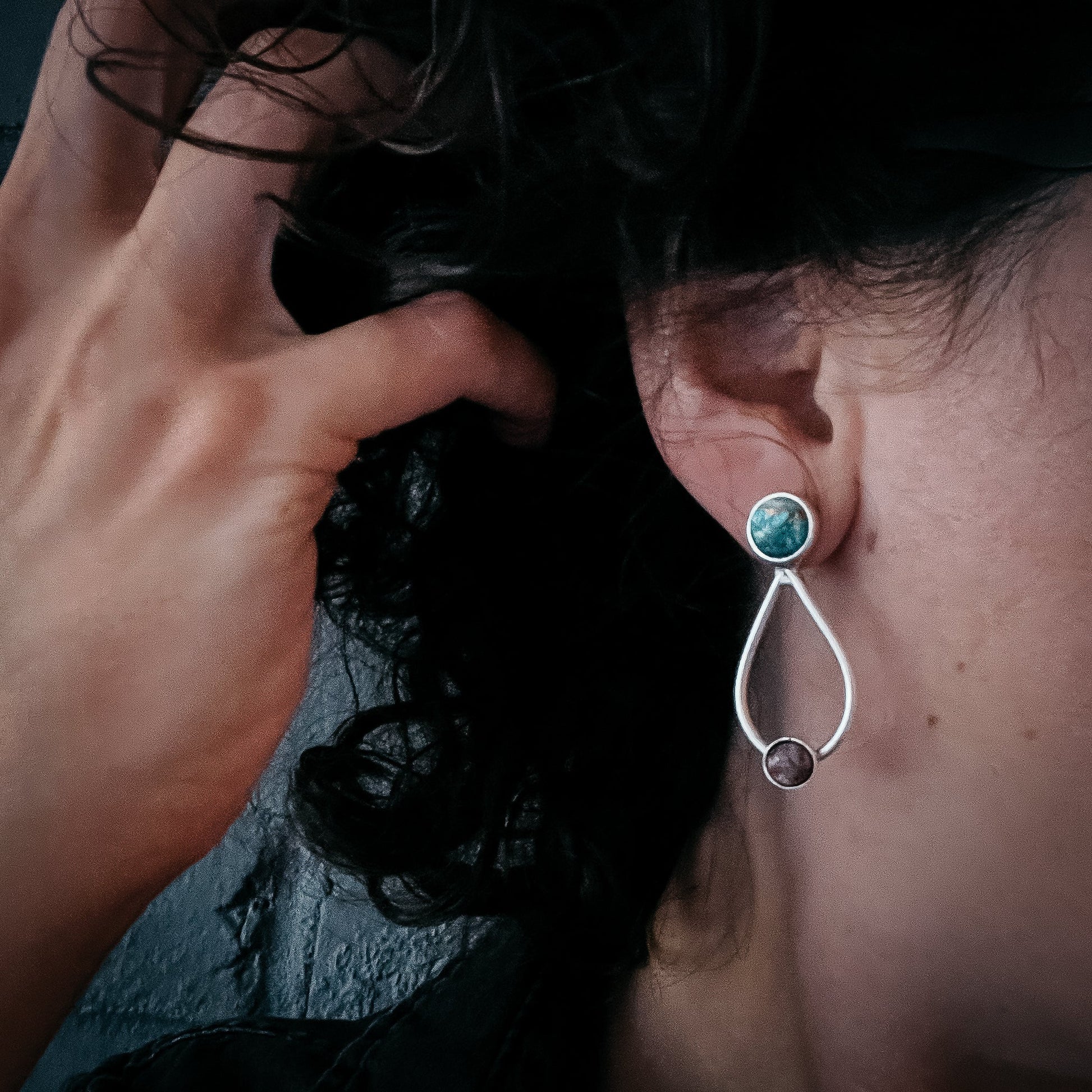 Close-up of an earring being worn, with a hand adjusting hair.