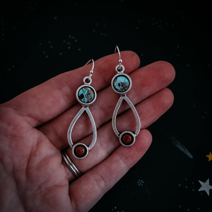 Silver earrings with gemstones held in a hand against a dark background