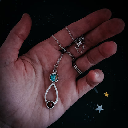 Hand holding a silver necklace with a turquoise pendant against a dark background