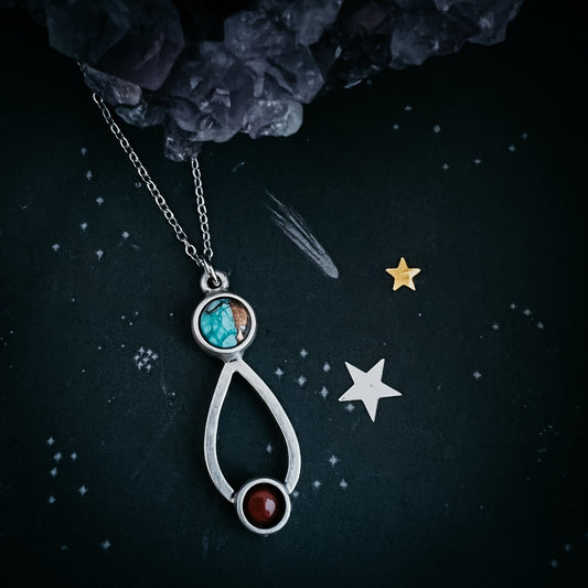 Silver necklace with a pendant featuring turquoise and red stones on a dark background with stars.