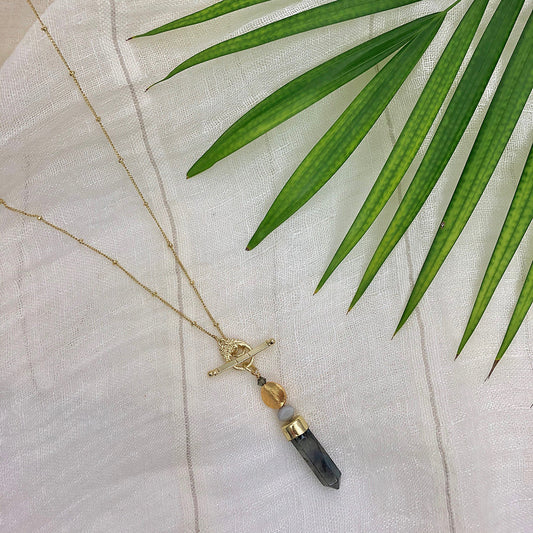 Necklace with a labradorite pendant on a white fabric background with green leaves