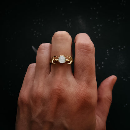Hand wearing a gold ring with a moonstone on a black background