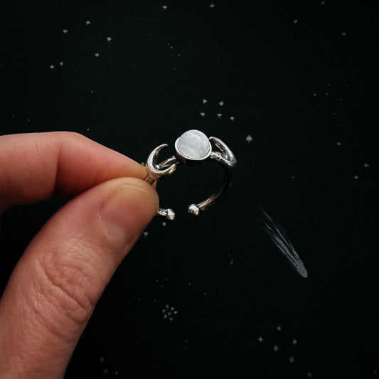 Silver ring with a central stone held by a hand against a black background