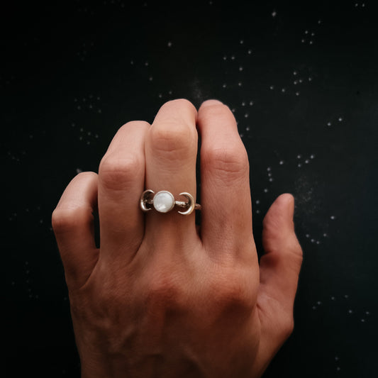 Hand wearing a gold ring with Moonstone against a dark background