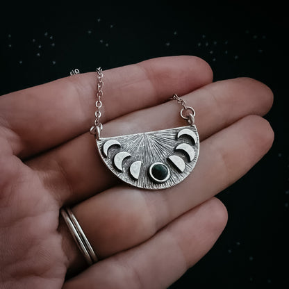 Silver necklace with a moon phase pendant held in a hand against a dark background