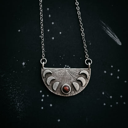 Silver necklace with a half-circle pendant featuring moon phases on a dark background