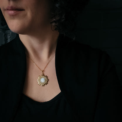 Woman wearing a gold necklace with a pendant against a dark background