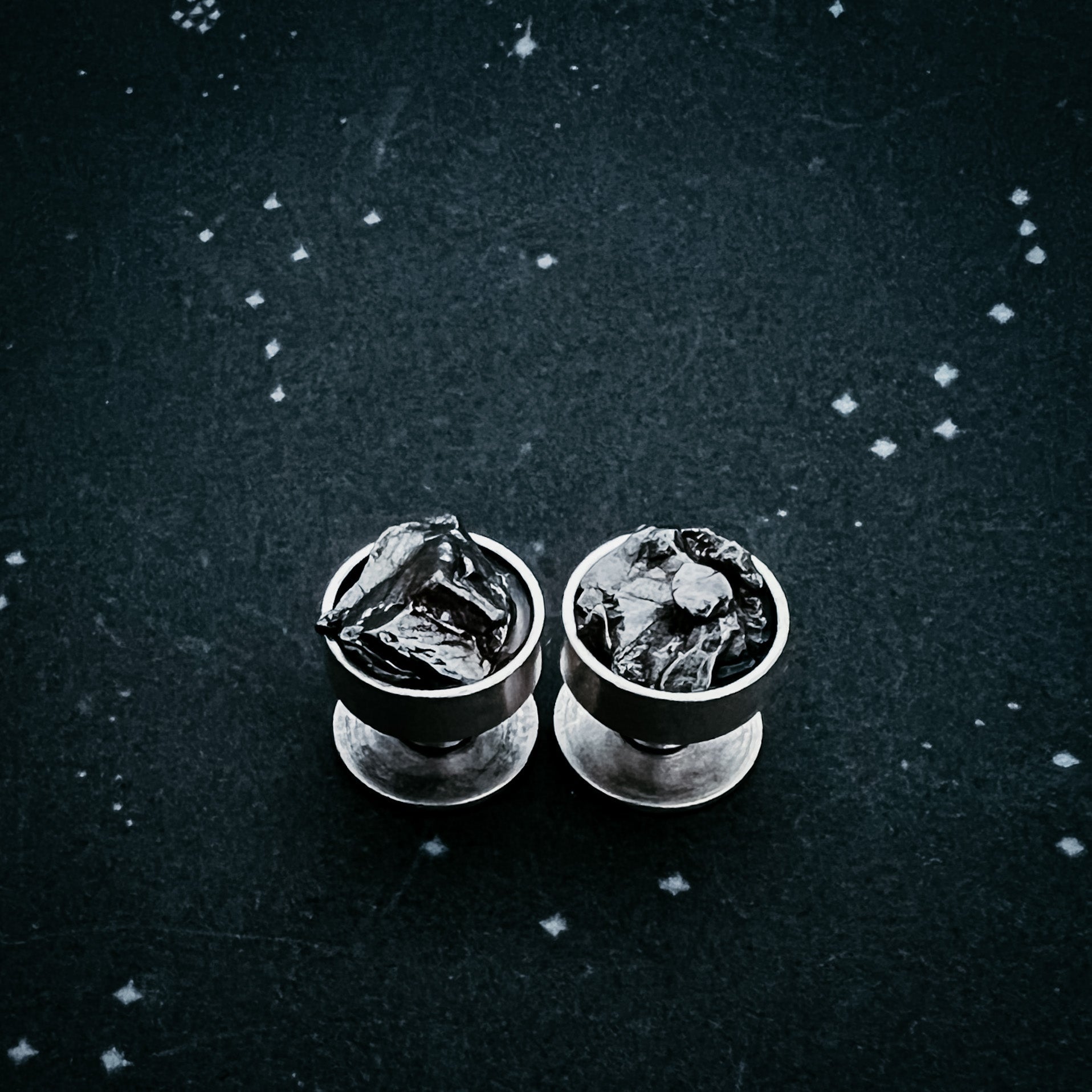 Two meteorite cufflinks on a textured black surface with star-like white dots.