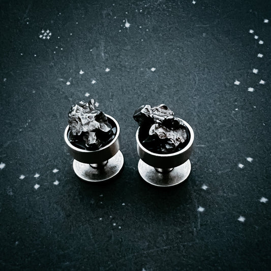 Two meteorite cufflinks with clear stones on a dark textured background