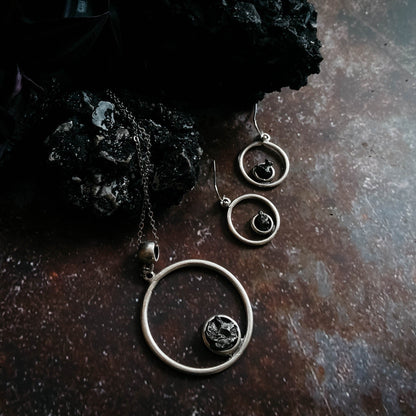 Pair of silver hoop earrings with central gemstone on a dark surface