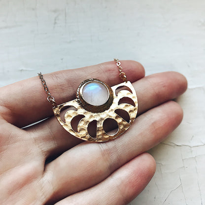 Gold necklace with a moonstone pendant held in a hand on a textured surface