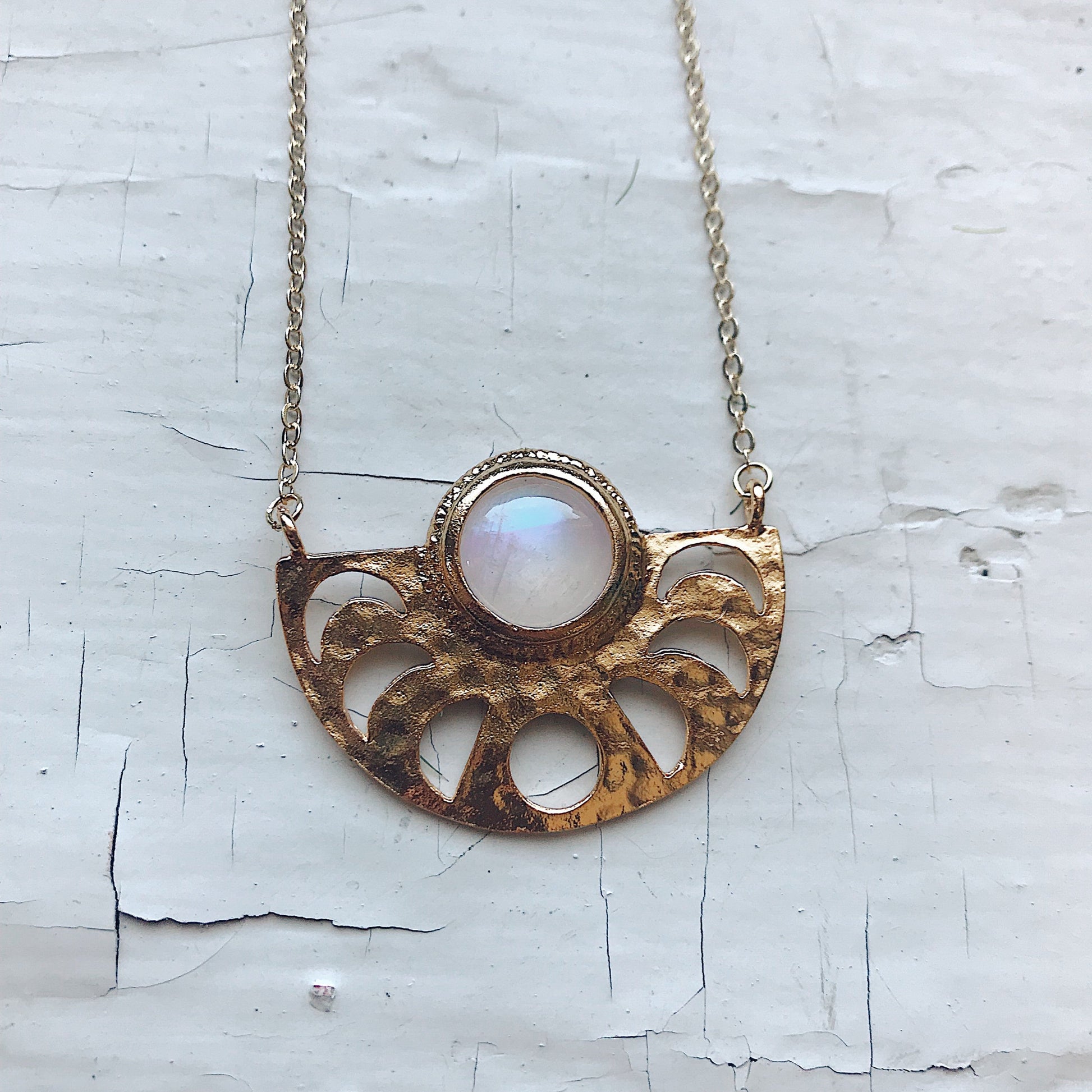 Gold necklace with a central gemstone on a textured white background