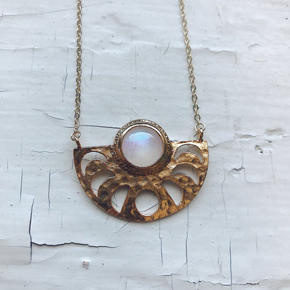 Gold necklace with a central gemstone on a textured white background