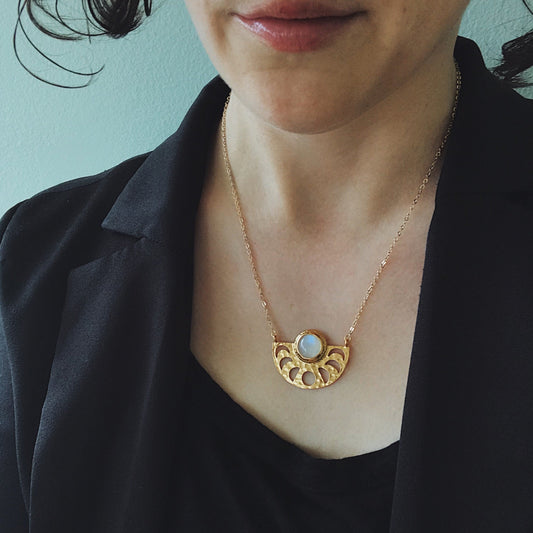 Woman wearing a gold necklace with a circular pendant against a light blue background