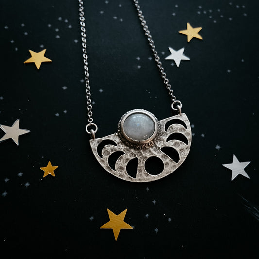 Silver necklace with a moonstone pendant on a black background with star decorations