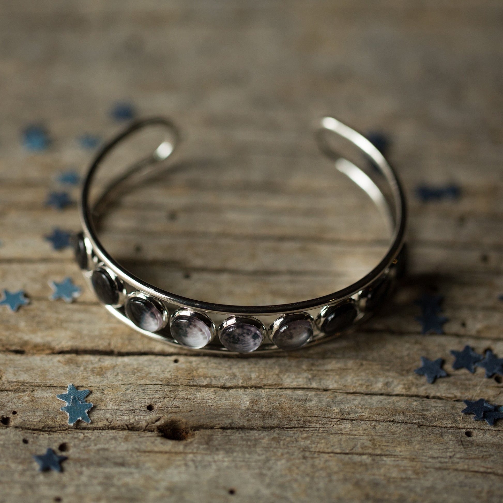 Silver bracelet with embedded stones on a wooden surface with scattered blue stars.