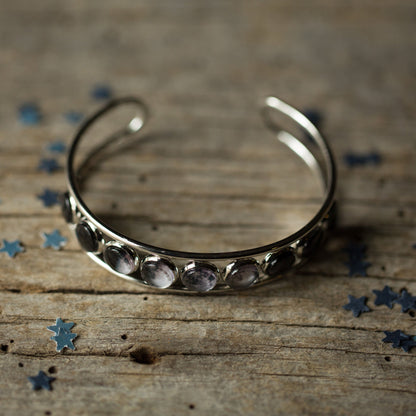 Silver bracelet with embedded stones on a wooden surface with scattered blue stars.