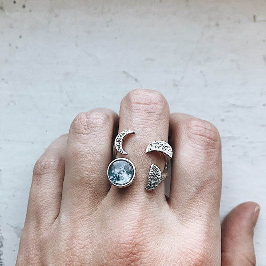 Hand wearing a silver ring with a moon design on a light background