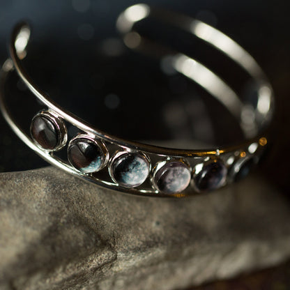 Silver adjustable cuff bracelet with embedded stones on a dark background