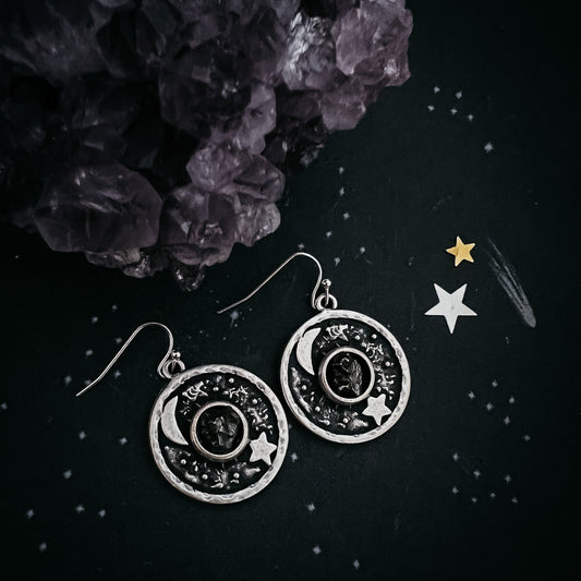 Silver celestial-themed earrings on a dark surface with decorative elements.