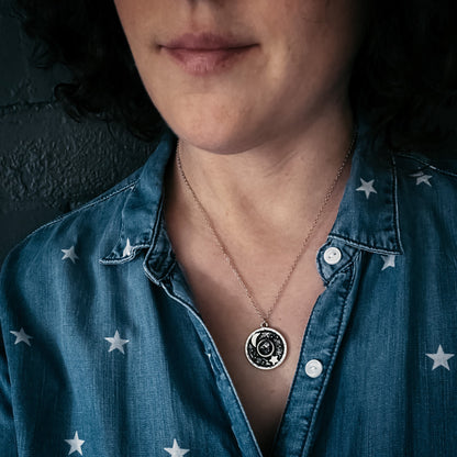 Woman wearing a blue denim shirt with star patterns and a necklace with a circular pendant.