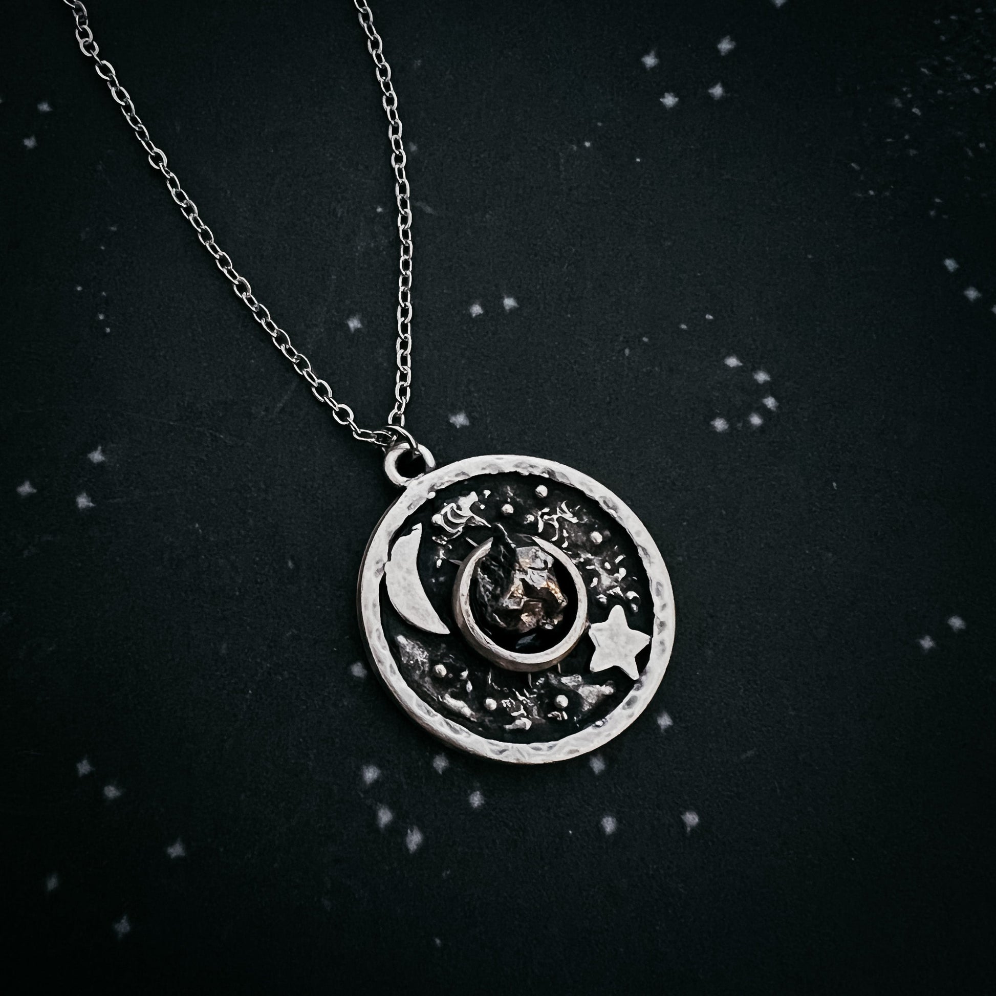 Silver necklace with a circular pendant featuring celestial designs on a black background.