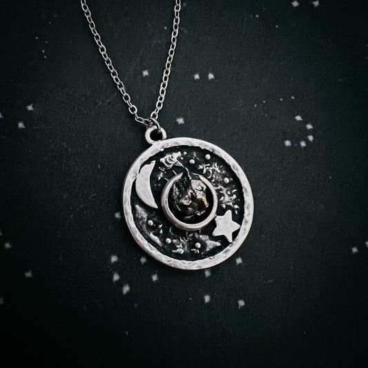 Silver necklace with a circular pendant featuring celestial designs on a dark background.