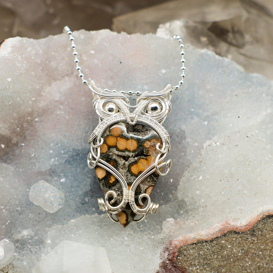 Silver owl-shaped ocean jasper pendant with a natural stone on a crystal background