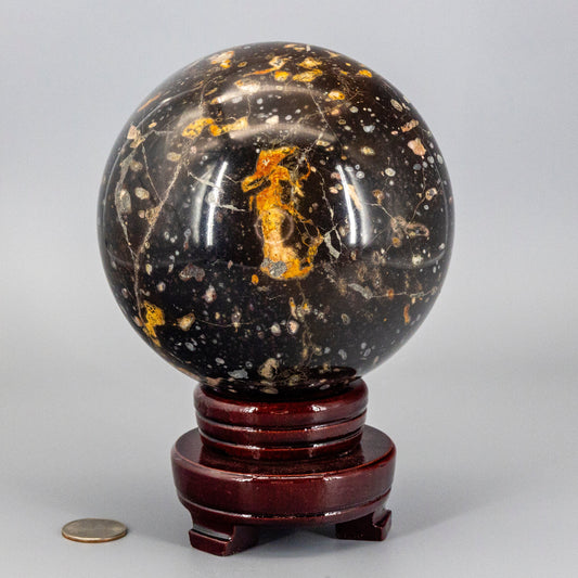 Decorative ocean jasper sphere with black and orange speckles on a wooden stand against a gray background