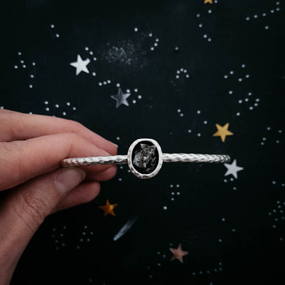 Silver bracelet with meteorite held by a hand against a starry night sky background