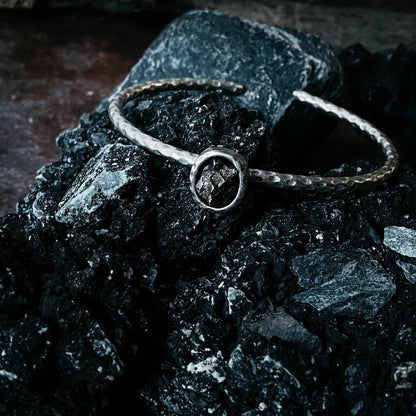 Silver bracelet with a meteorite on a dark surface.