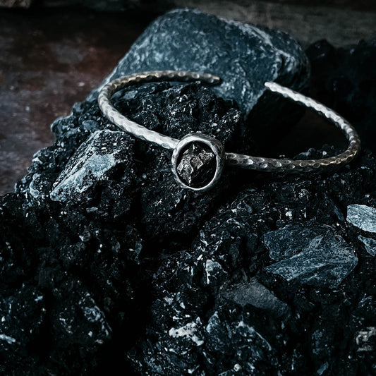 Silver bracelet with a meteorite on a dark surface.