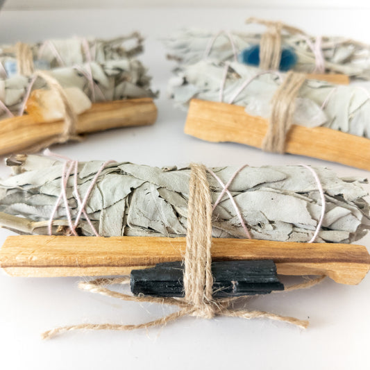 Bundles of sage, palo santo and crystals tied with twine on a white surface