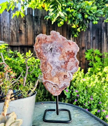 Geode crystal on a stand in a garden setting with plants and a wooden fence.