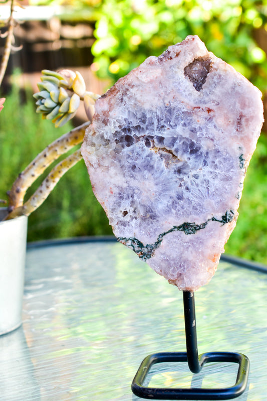 Pink amethyst geode crystal on a stand with a plant in the background