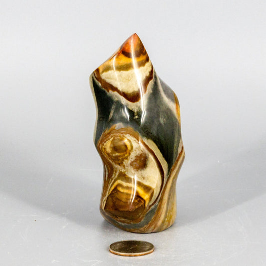 Decorative polychrome jasper flame stone with a coin for scale on a white background