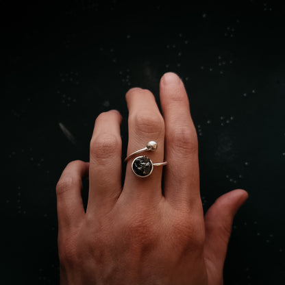 Hand wearing a ring with meteorite on a black background
