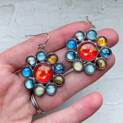 Colorful celestial-themed earrings held in a hand against a light background