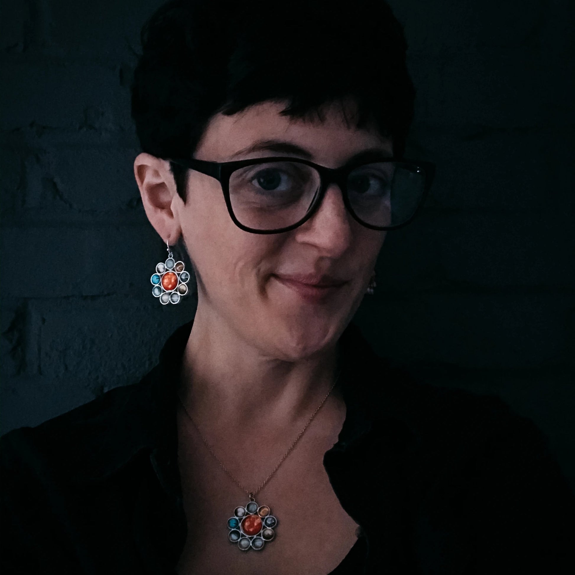 Woman wearing glasses and colorful earrings against a dark background