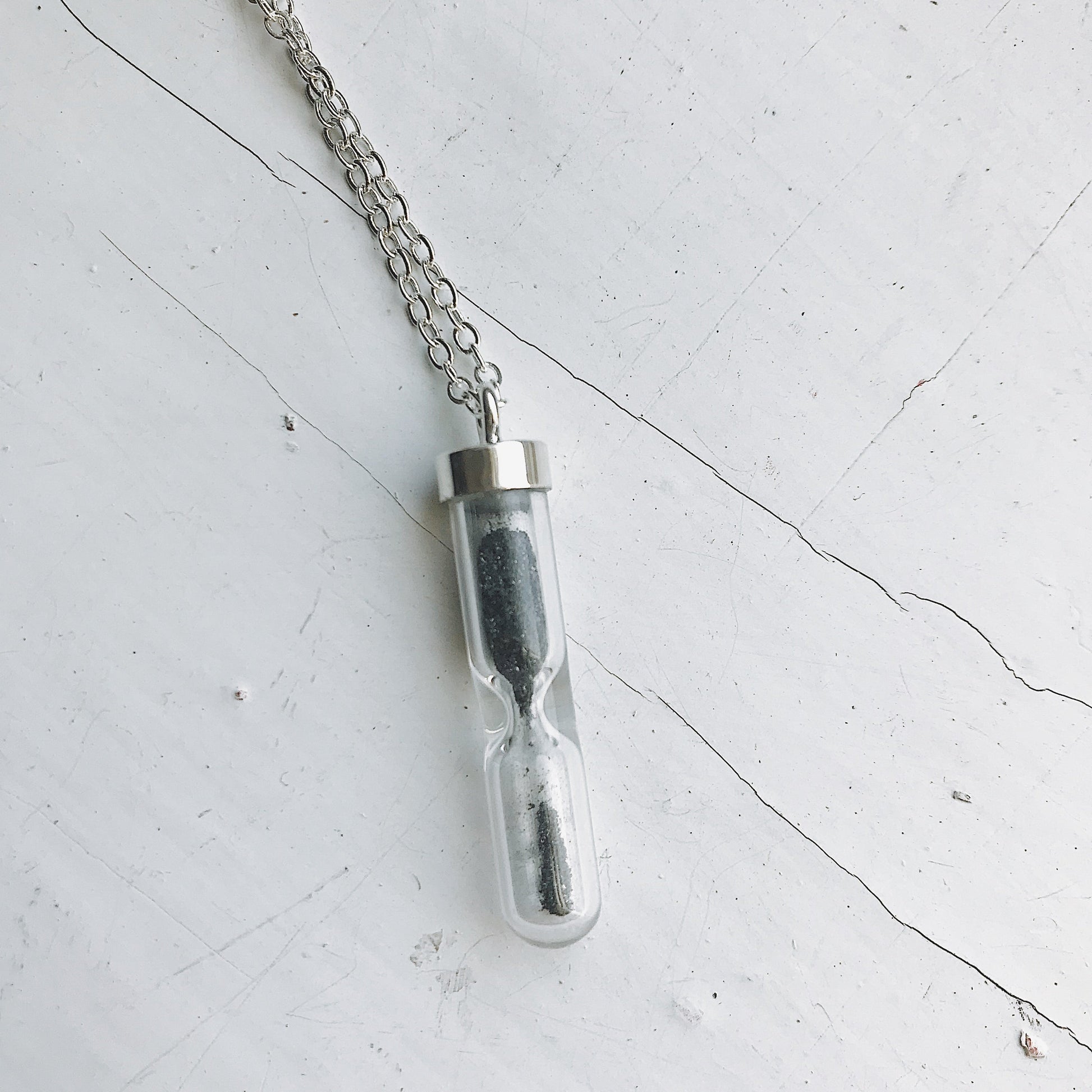 Glass vial necklace with chain on a light gray surface