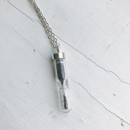 Glass vial necklace with chain on a light gray surface