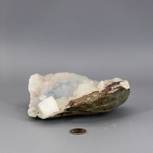 Rare chalcedony quartz cluster on a gray background with a coin for scale
