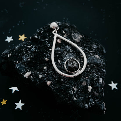 Silver teardrop-shaped pendant on a dark stone surface with decorative stars.