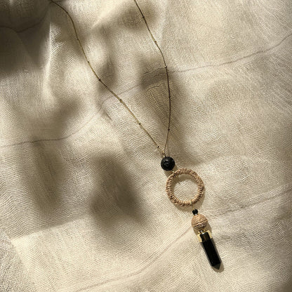 Necklace with black beads and circular pendant on a textured beige fabric background
